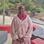 Wearing a headscarf, Ikran stands in the middle of school grounds smiling