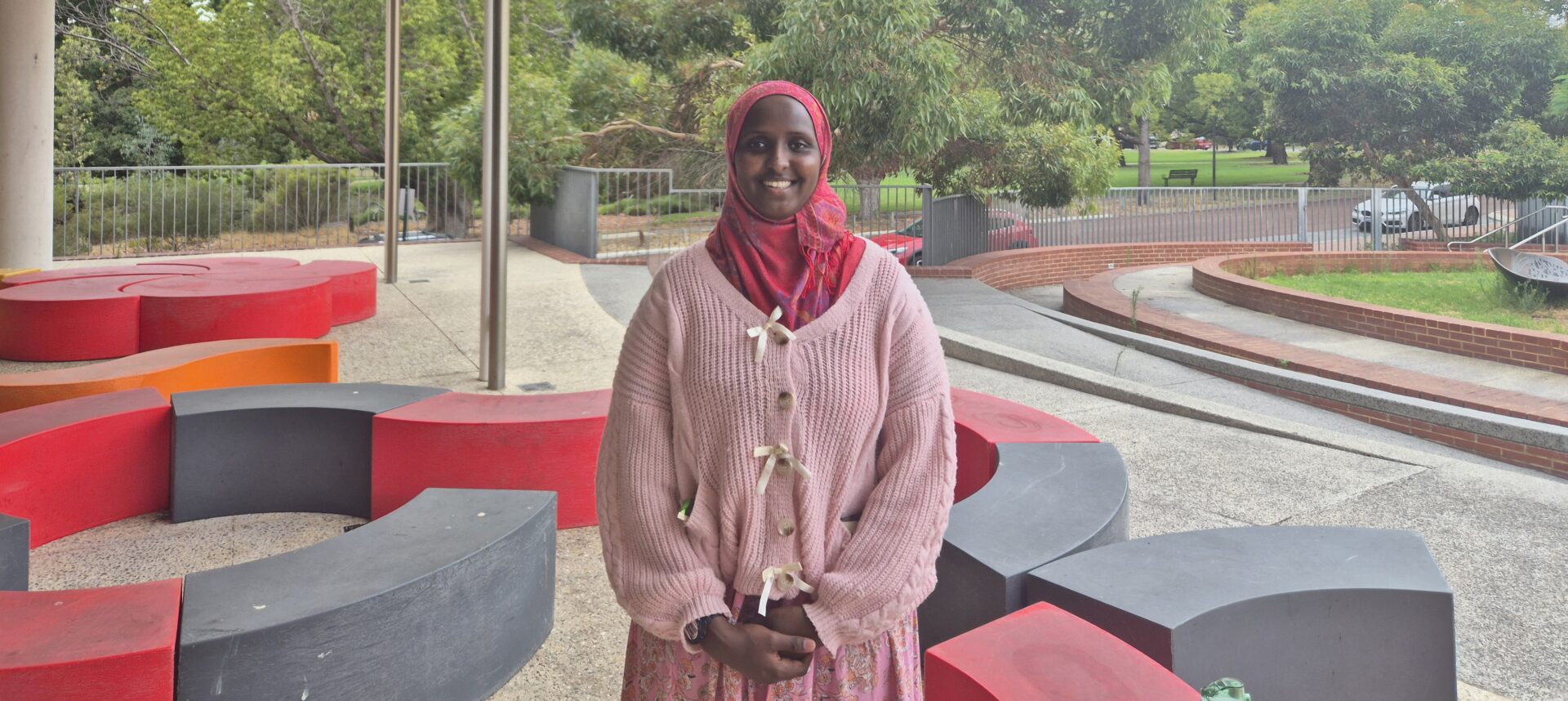 Wearing a headscarf, Ikran stands in the middle of school grounds smiling 